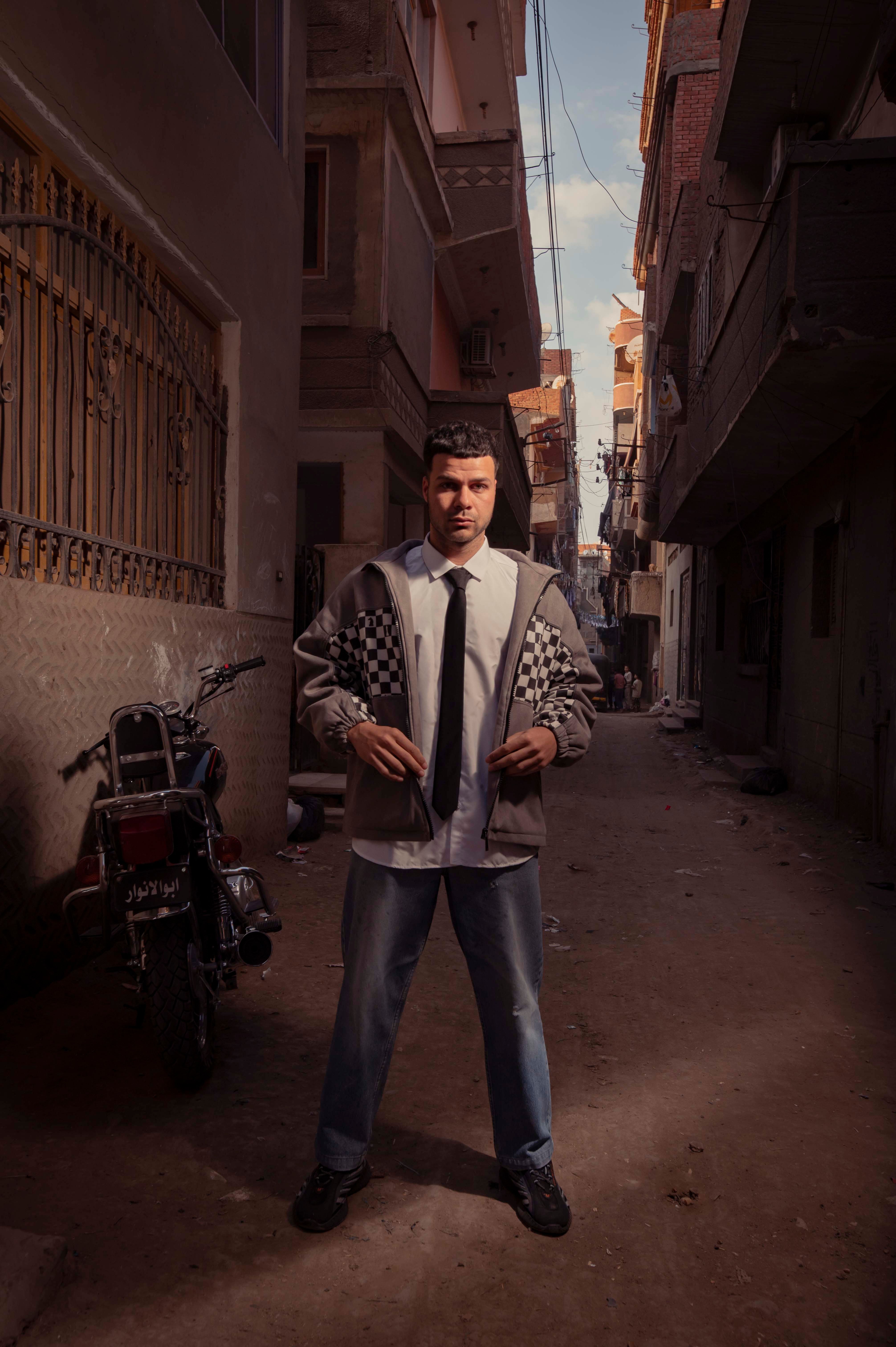Stylish man posing in urban alley, showing modern fashion with a tiled jacket.