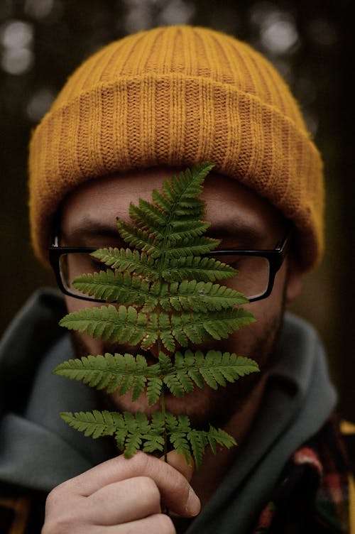 A man in a beanie and glasses is holding a fern leaf