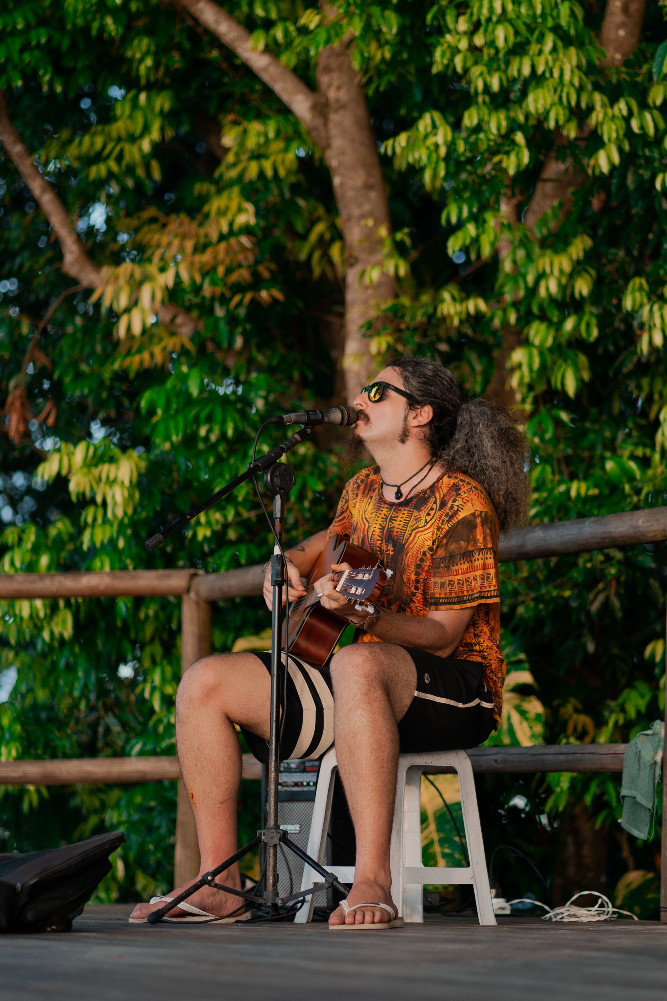 Musician playing guitar and singing outdoors among trees.