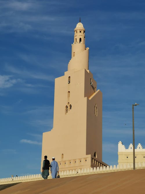Two people walk past a tall tower with a clock on it