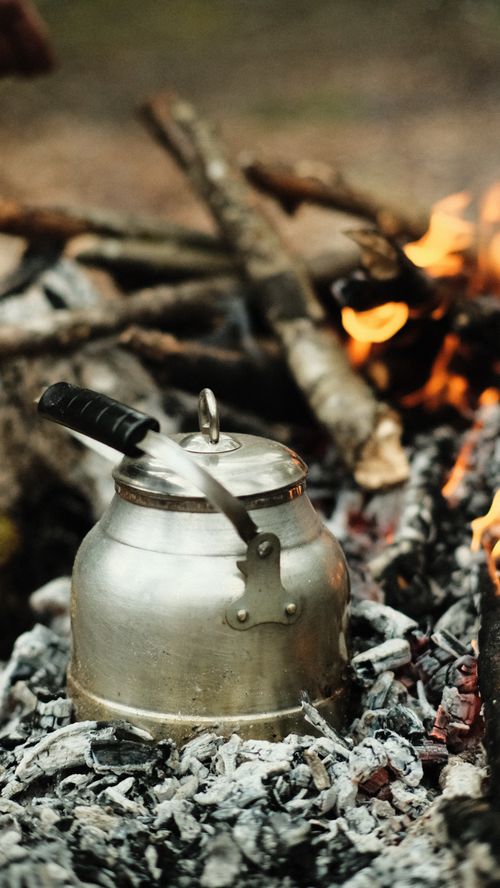 Free Metal kettle on campfire with burning logs and ash for outdoor cooking. Stock Photo