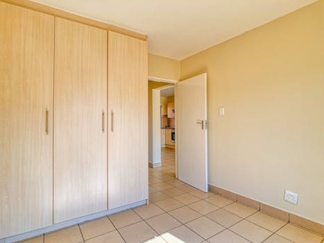 Bright, minimalist interior with tile flooring and a wooden wardrobe in Pretoria, South Africa.