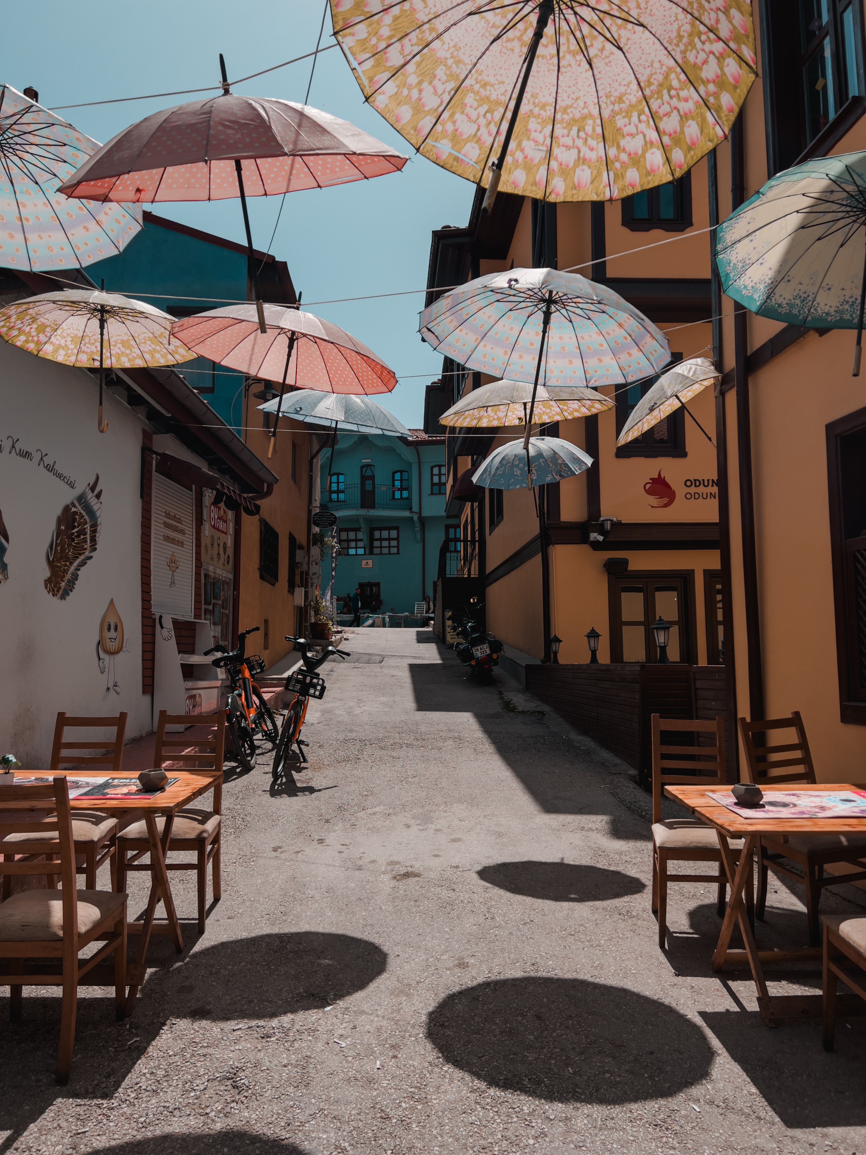 Quaint alleyway with colorful umbrellas, tables, and chairs in a small town setting.