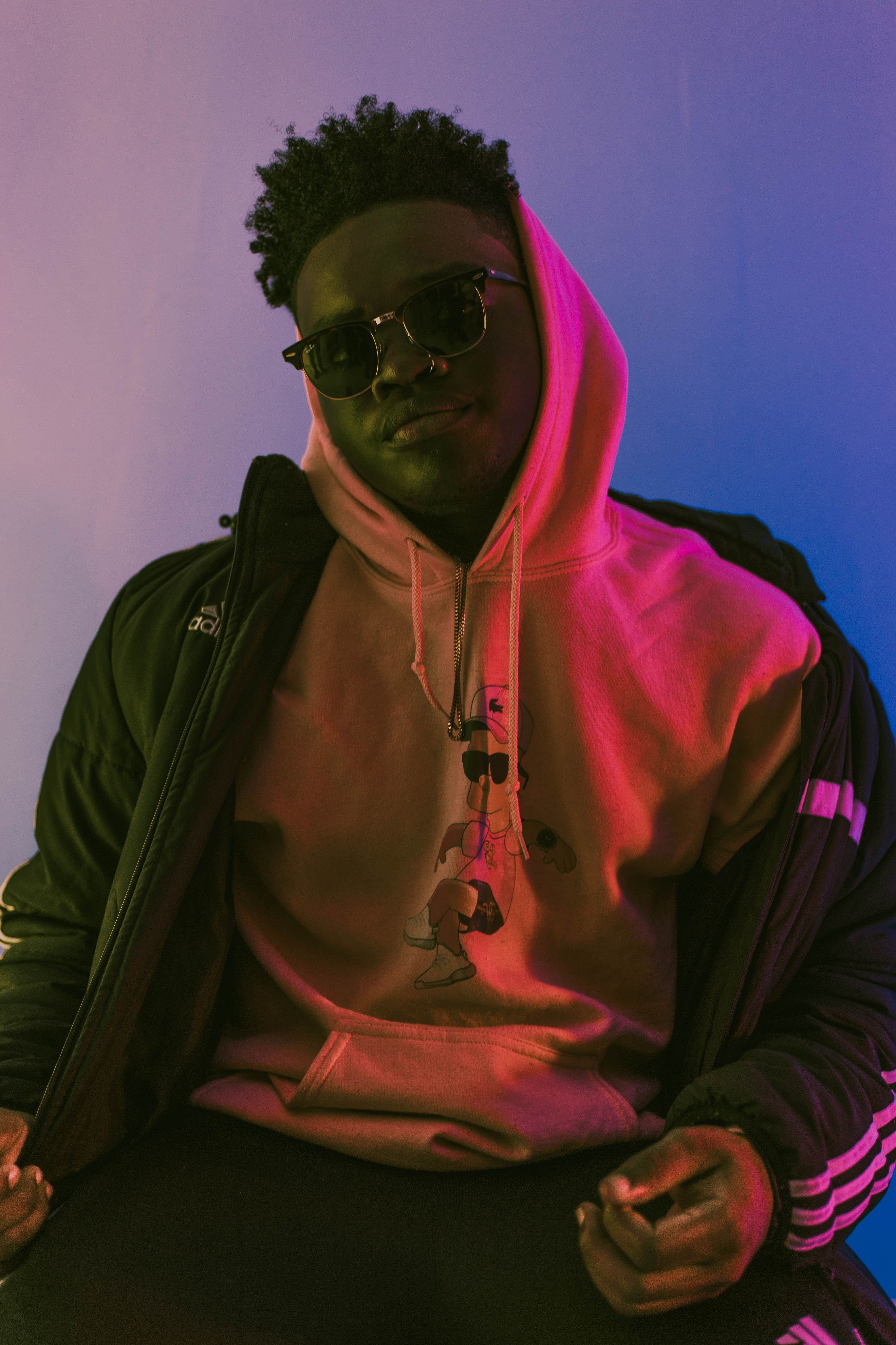 Portrait of a young man in a hoodie and sunglasses with cool lighting for a modern street style vibe.