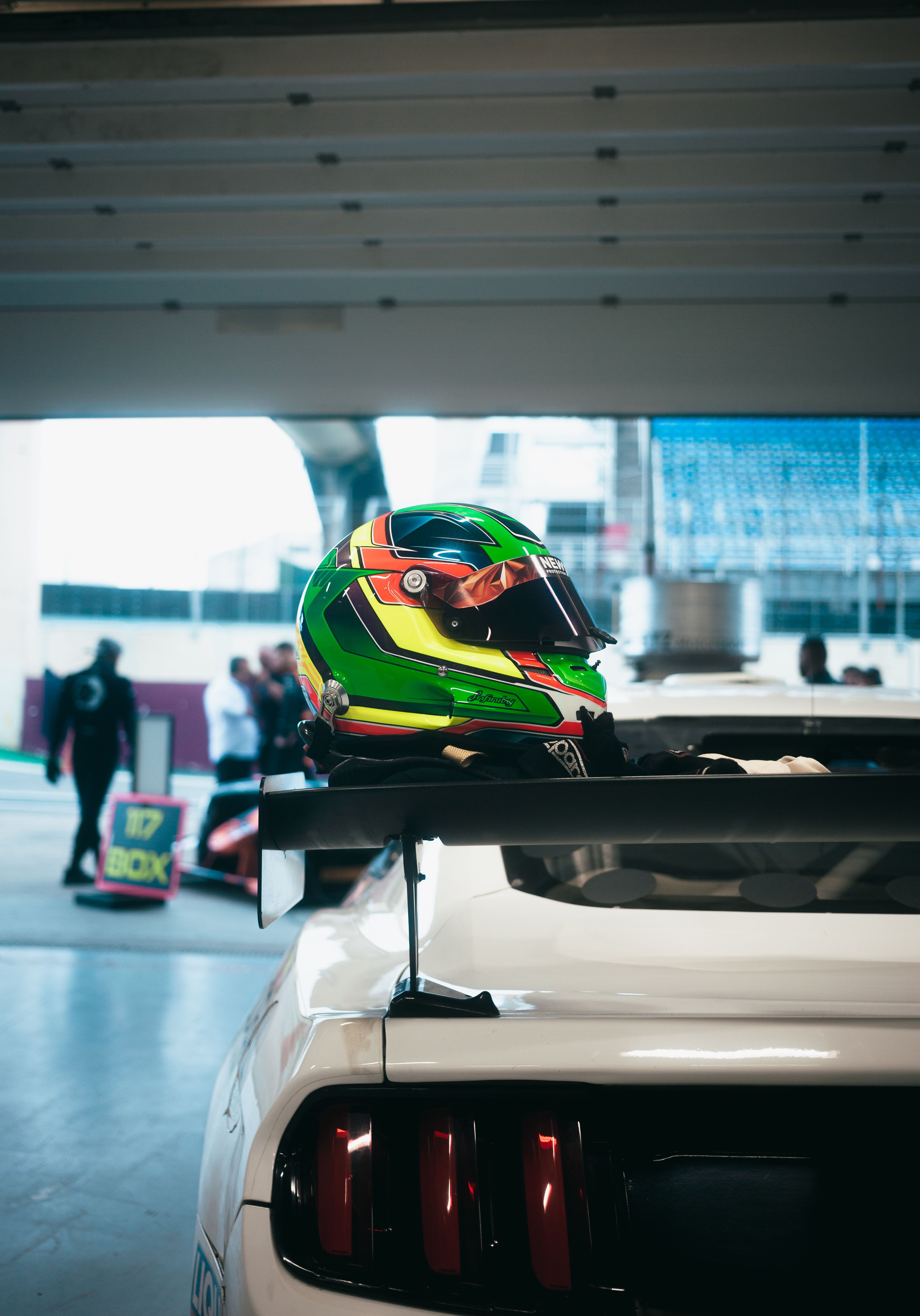 A colorful racing helmet rests on a car spoiler indoors at a motorsport event.