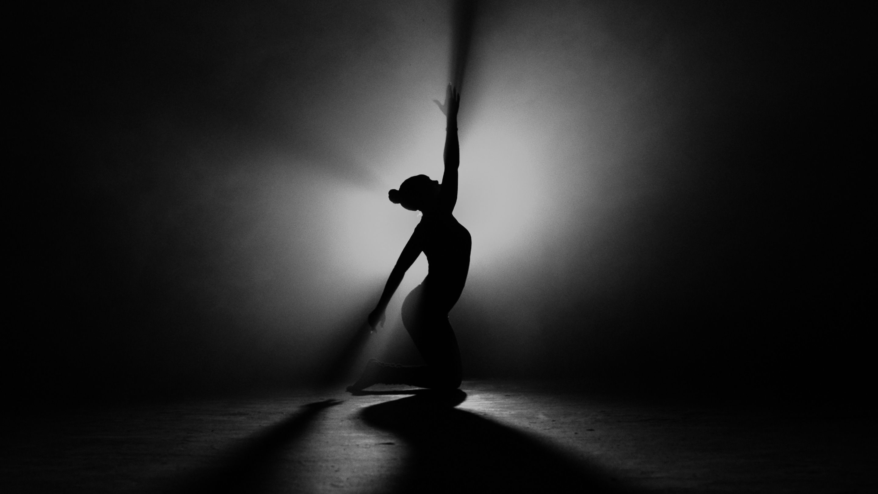 silhouette of a person kneeling in a dark room with a single beam of light