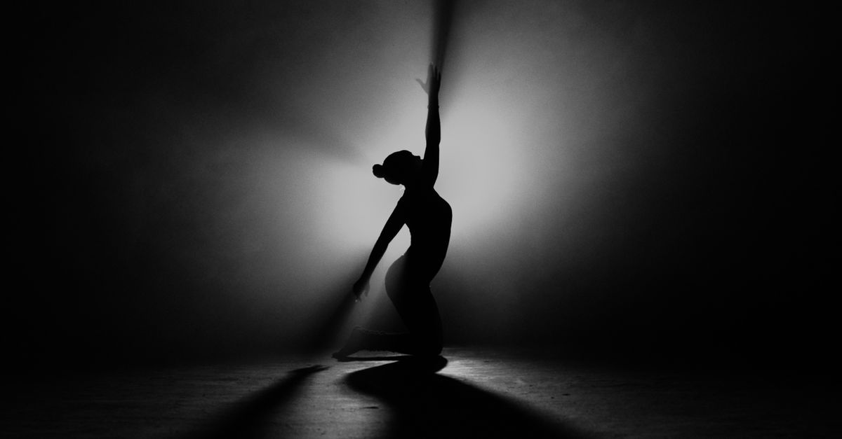 silhouette of a person kneeling in a dark room with a single beam of light