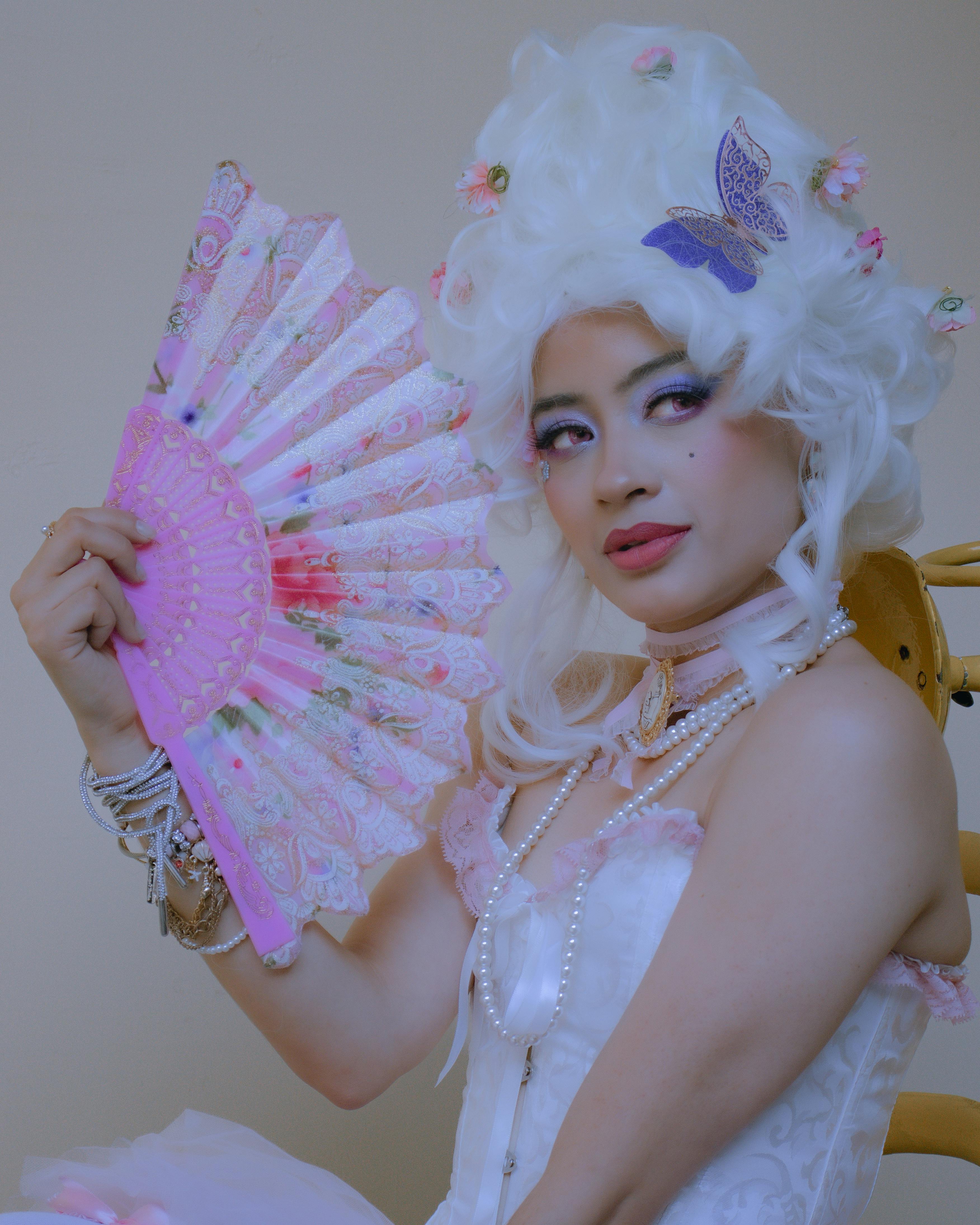 Elegant portrait of a woman with a floral fan and rococo-inspired attire, showcasing vintage fashion and charm.