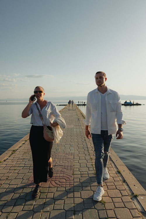 A man and woman walking on a pier near water