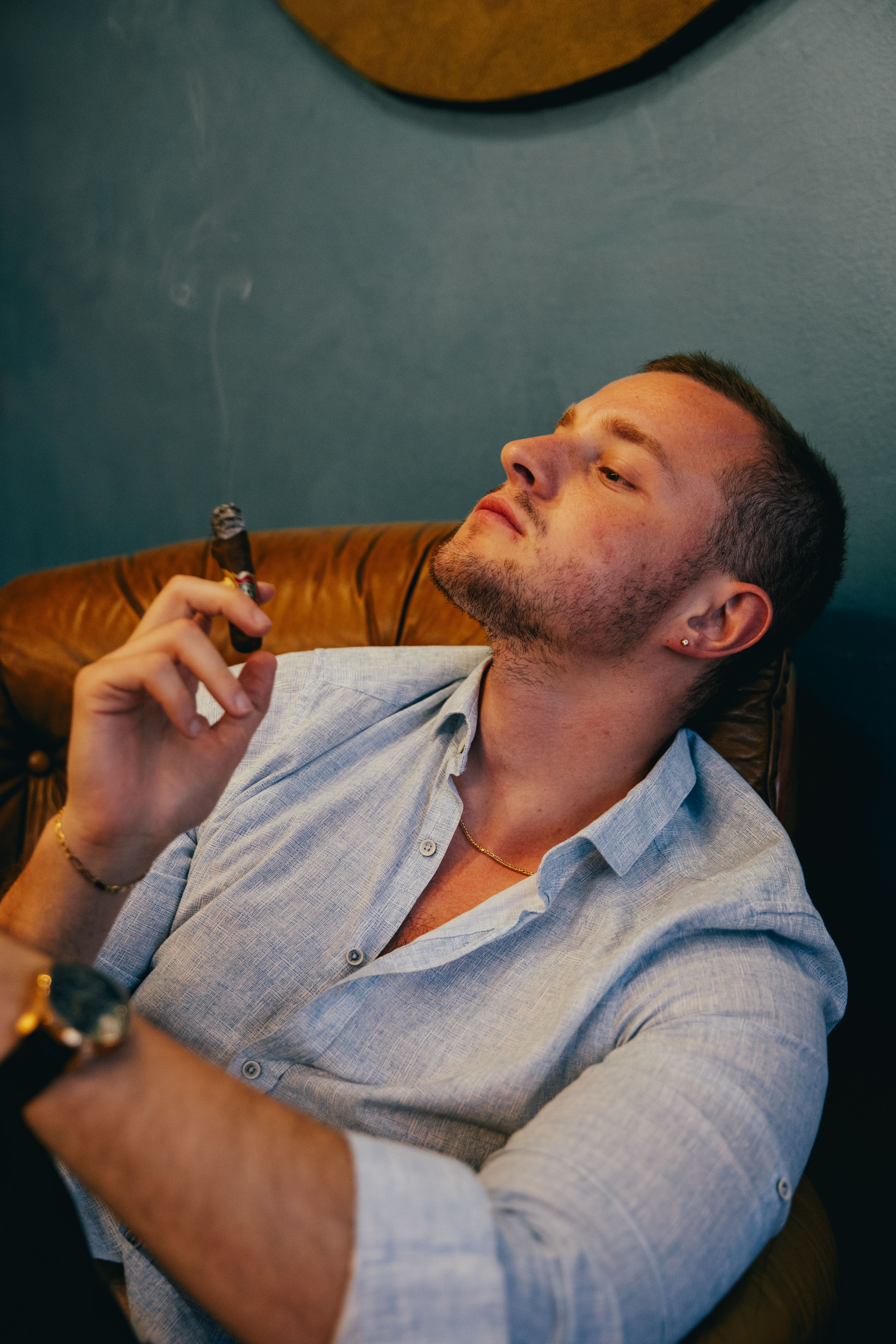 A sophisticated man enjoying a cigar in a relaxed indoor setting.