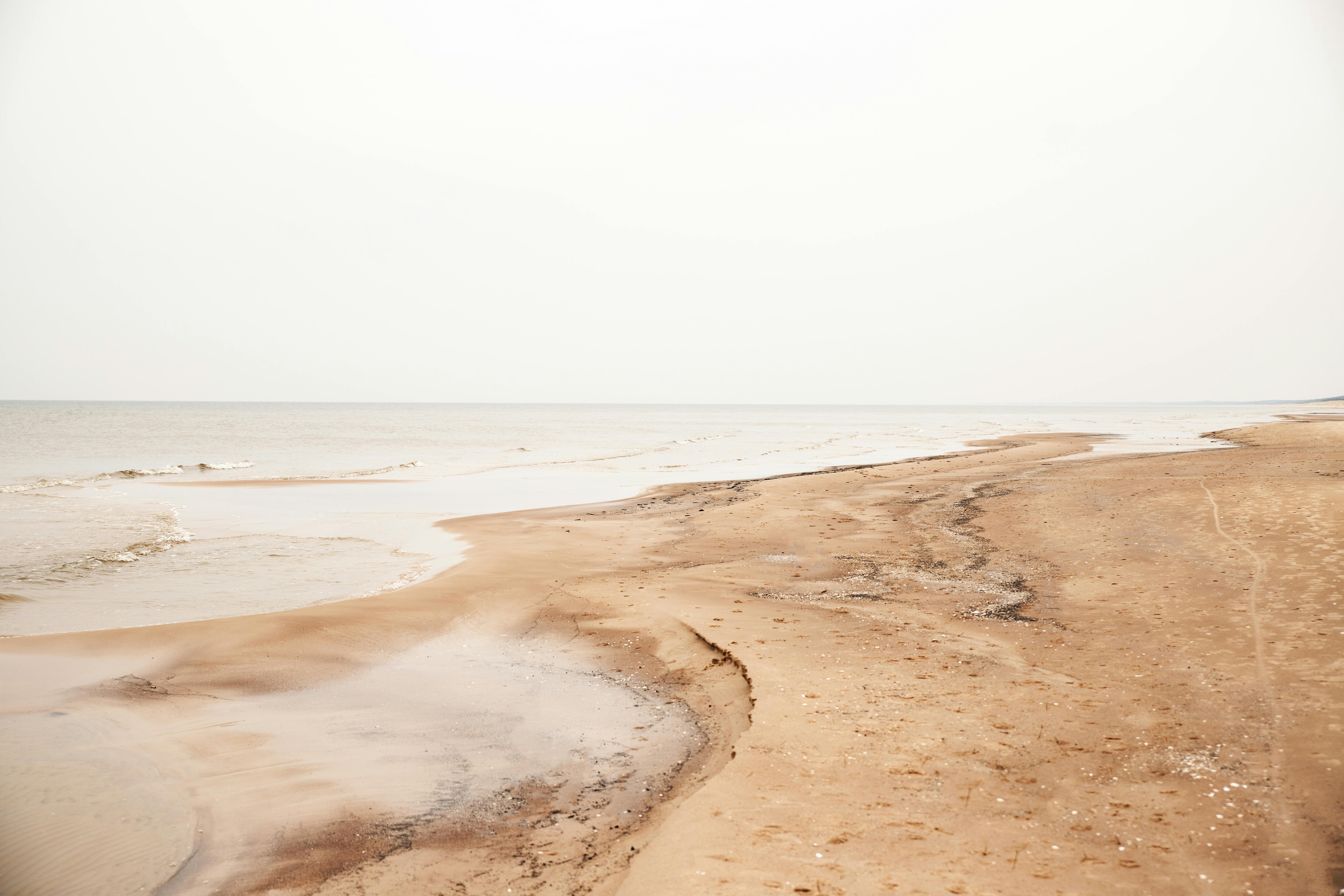 A serene view of Liepāja's sandy coast under an overcast sky, capturing tranquility.