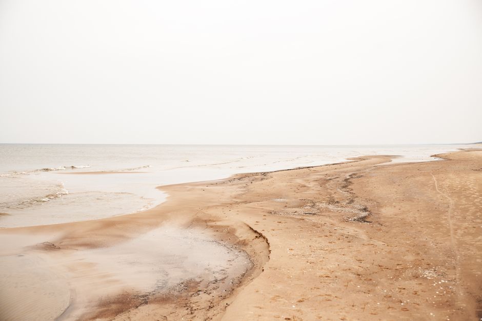 A serene view of Liepāja's sandy coast under an overcast sky, capturing tranquility.