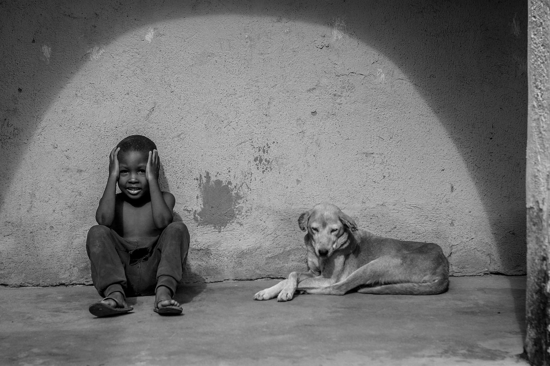 A boy and a dog sit in front of a wall