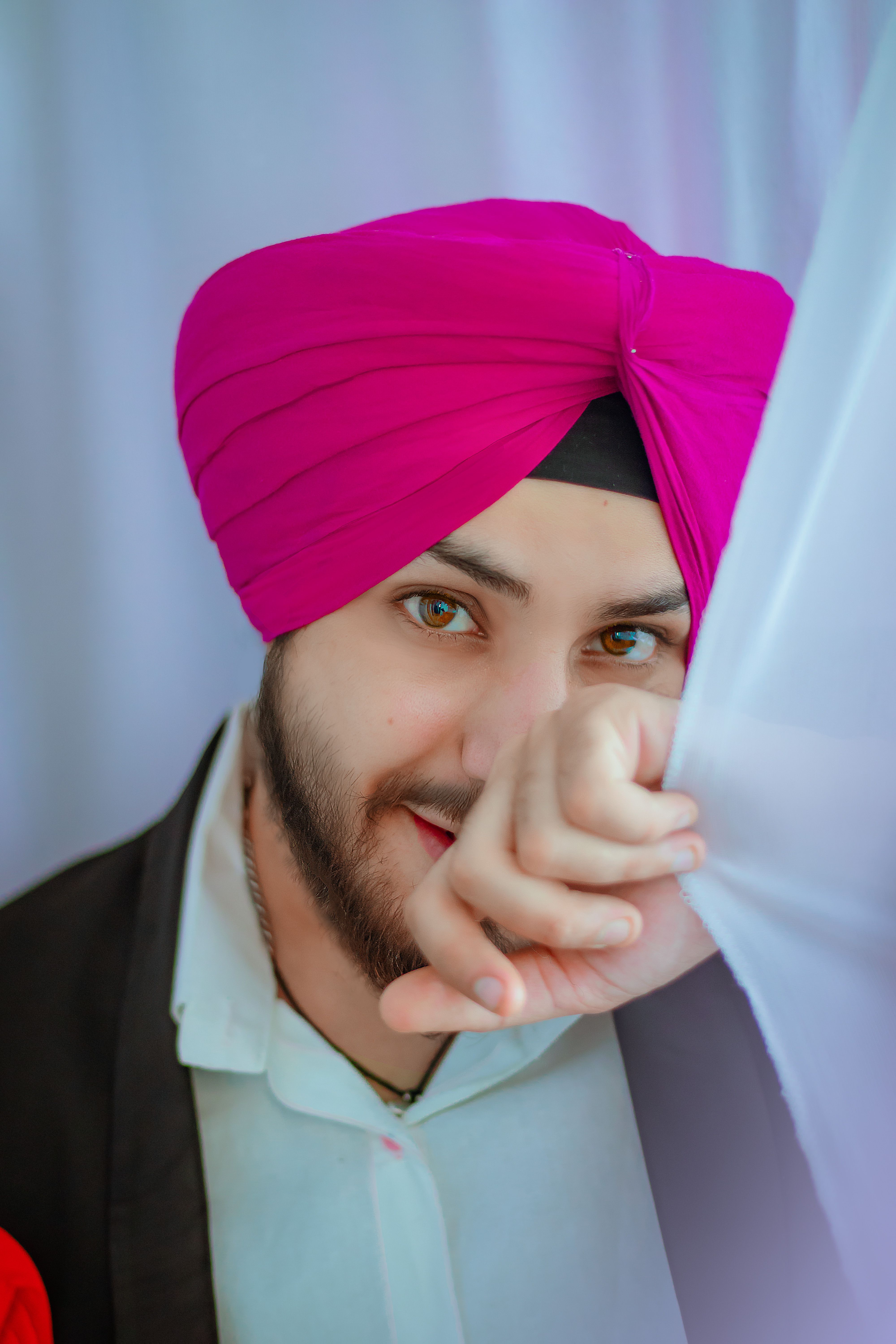 A fashionable man with a beard smiling, wearing a pink turban, posing indoors.