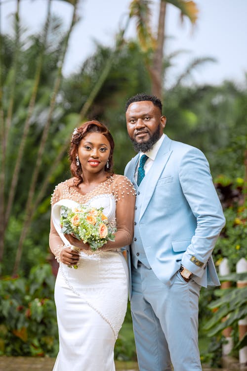 A bride and groom pose for a photo in front of palm trees