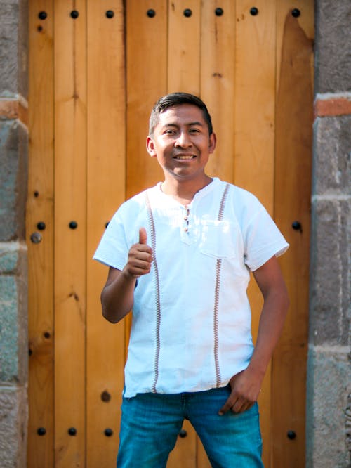 A man in a white shirt and jeans is giving the thumbs up