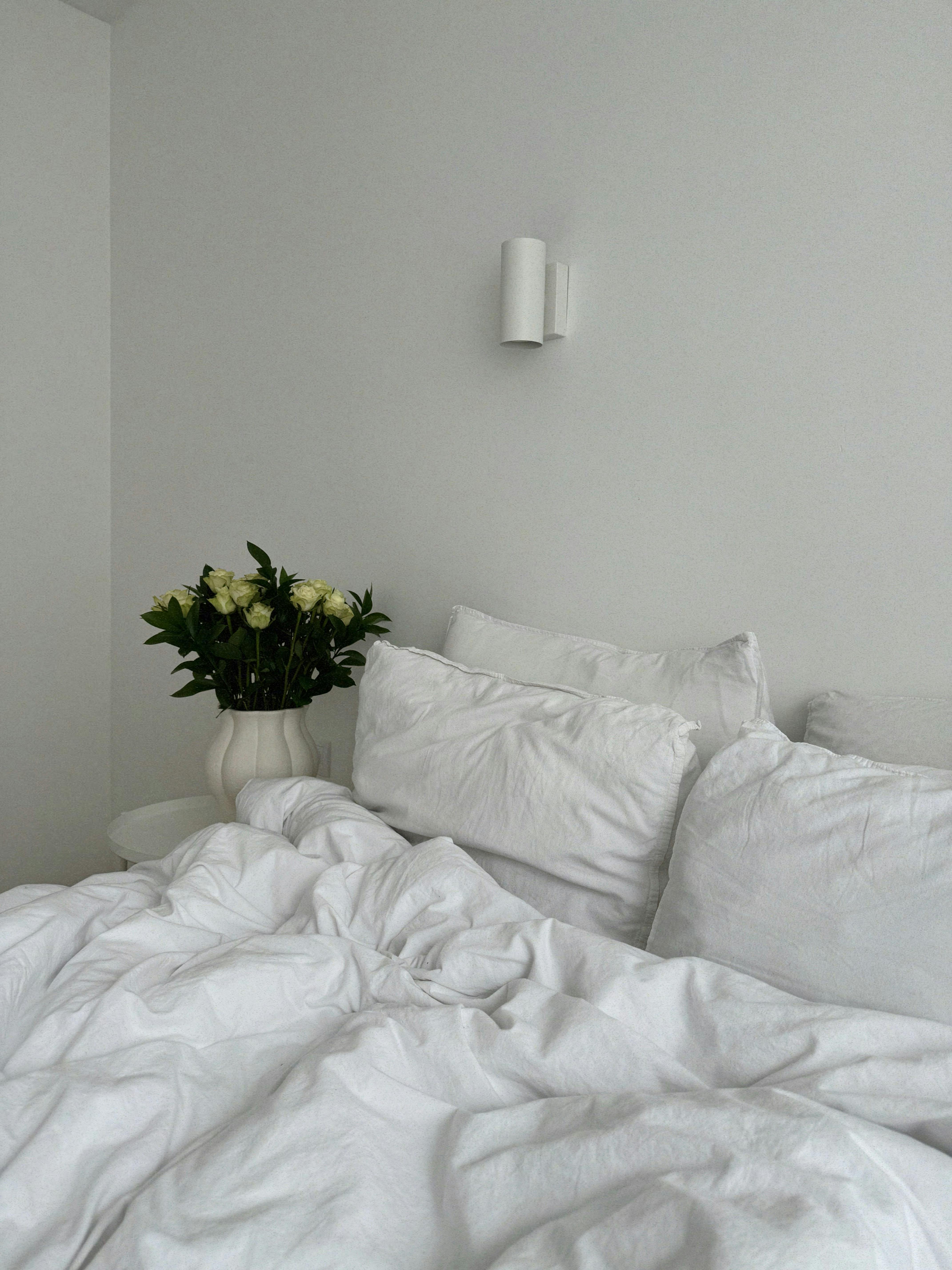 A tranquil bedroom scene featuring elegant white bedding and a vase of white roses.