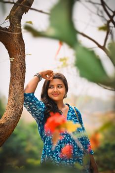 Charming woman in a blue dress smiling under a tree in Kolkata, India. 21706037