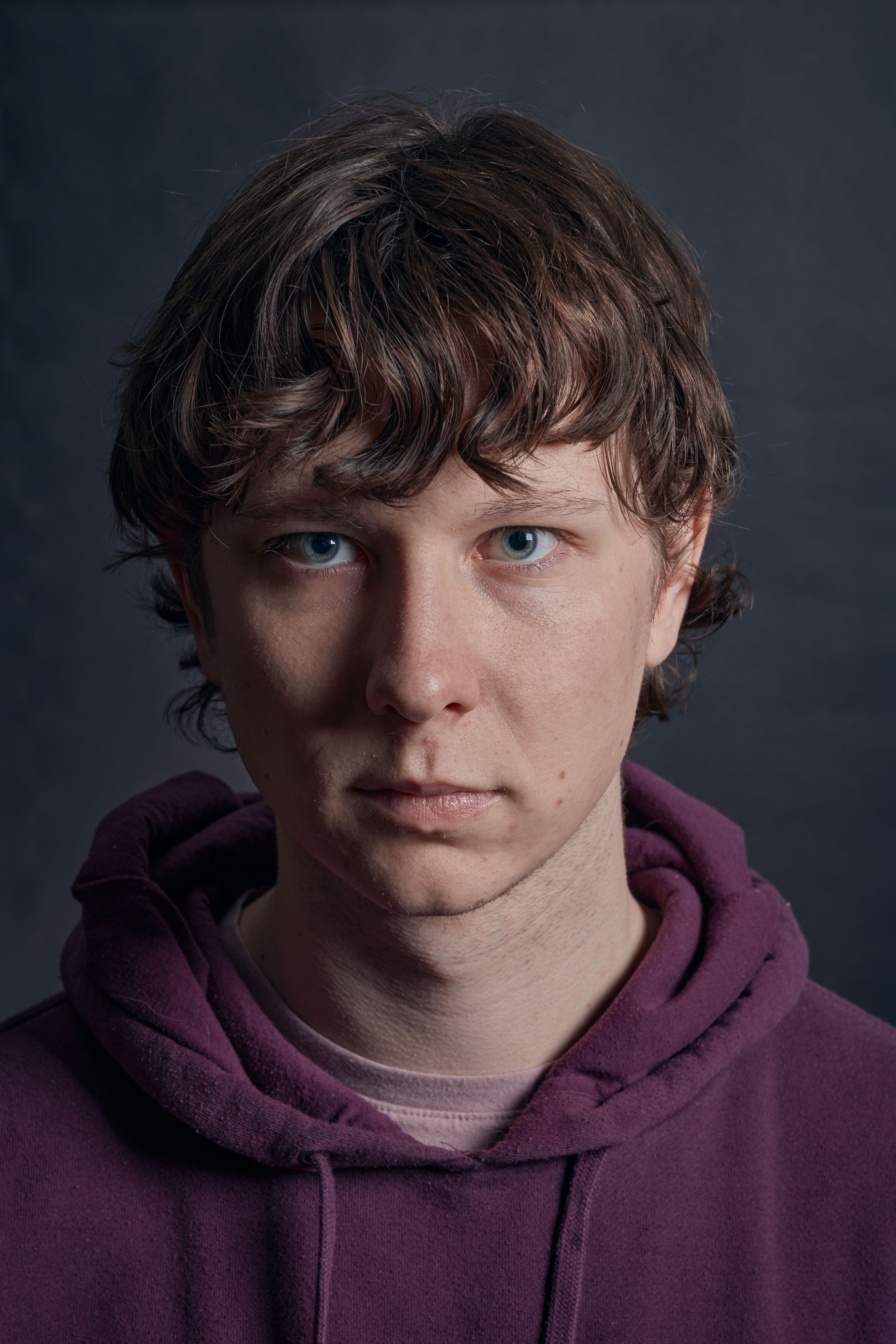 Portrait of a man with brown hair in a studio, wearing a purple hoodie.