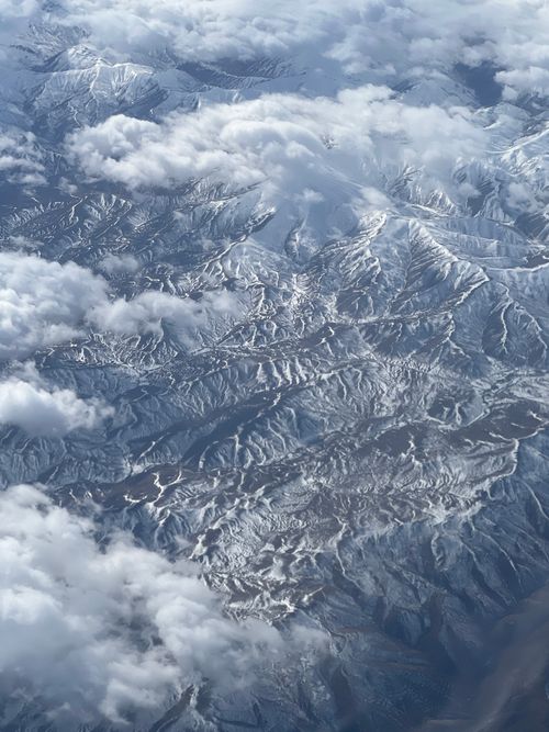 Free High altitude aerial view of a snow-covered mountain range obscured by clouds. Stock Photo