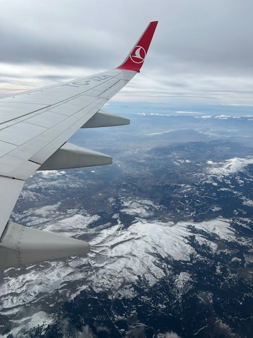 A view of the wing of an airplane flying over snow covered mountains