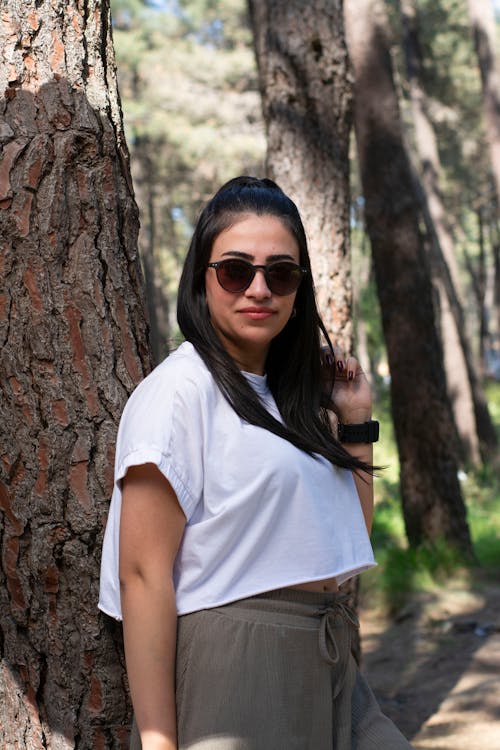 Free A woman in a white shirt and sunglasses standing in front of a tree Stock Photo