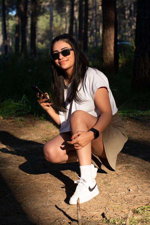 Free A woman crouching down in the woods with her phone Stock Photo