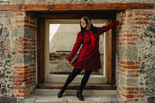 Free A stylish woman poses joyfully in a red jacket by a rustic stone wall, radiating happiness. Stock Photo