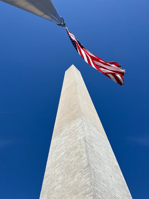 The washington monument is seen with an american flag