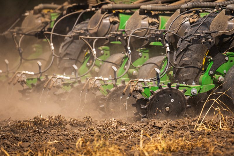 Close-up of modern agricultural machinery sowing seeds on a dusty field
