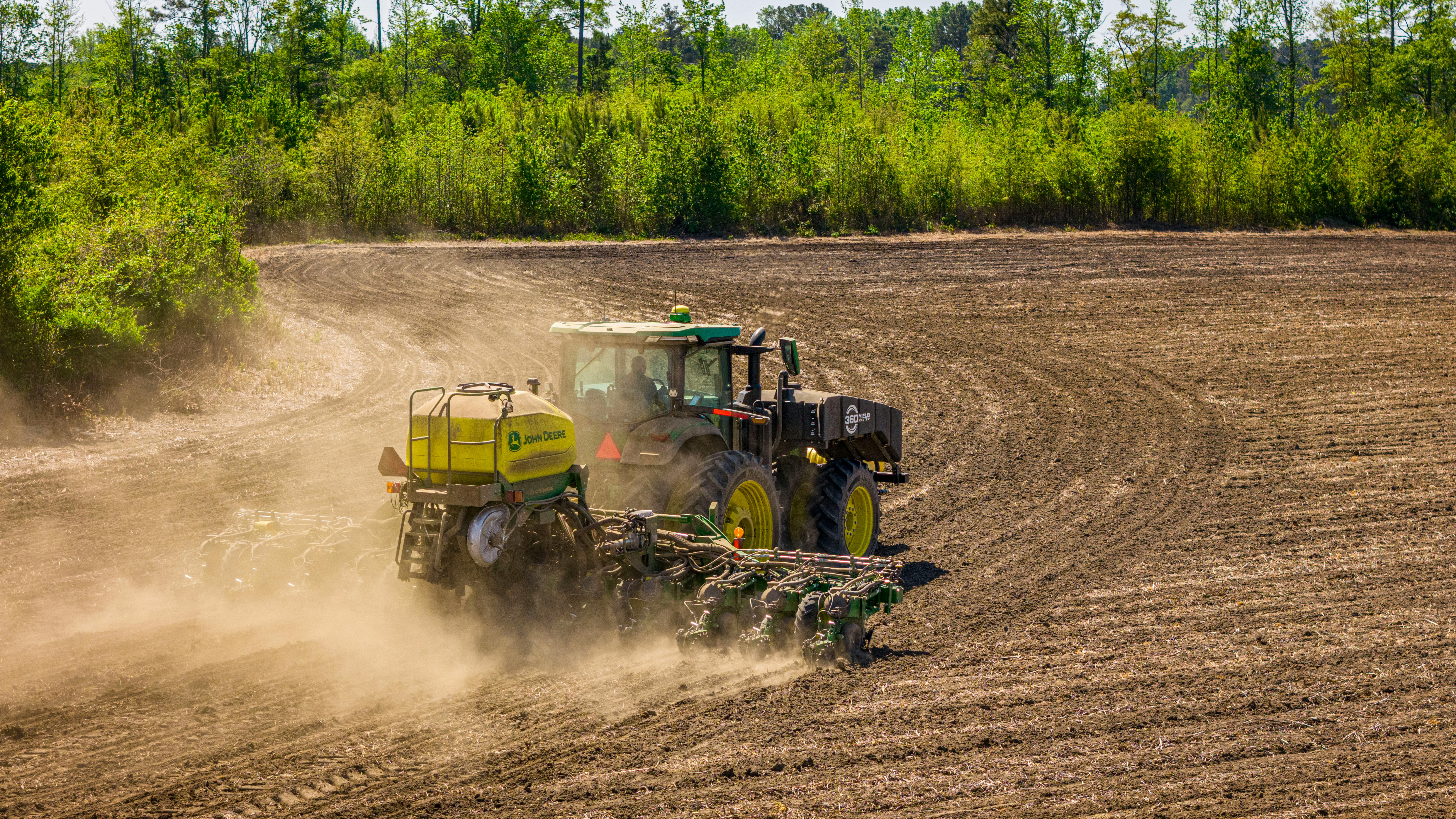 A tractor tills a vast field in rural North Carolina, surrounded by dense greenery.