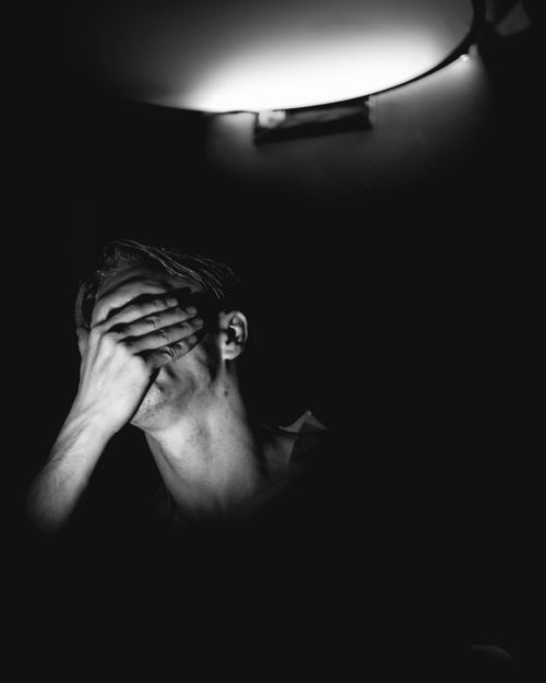 Free Dramatic black and white portrait of a man covering his face under soft light. Stock Photo