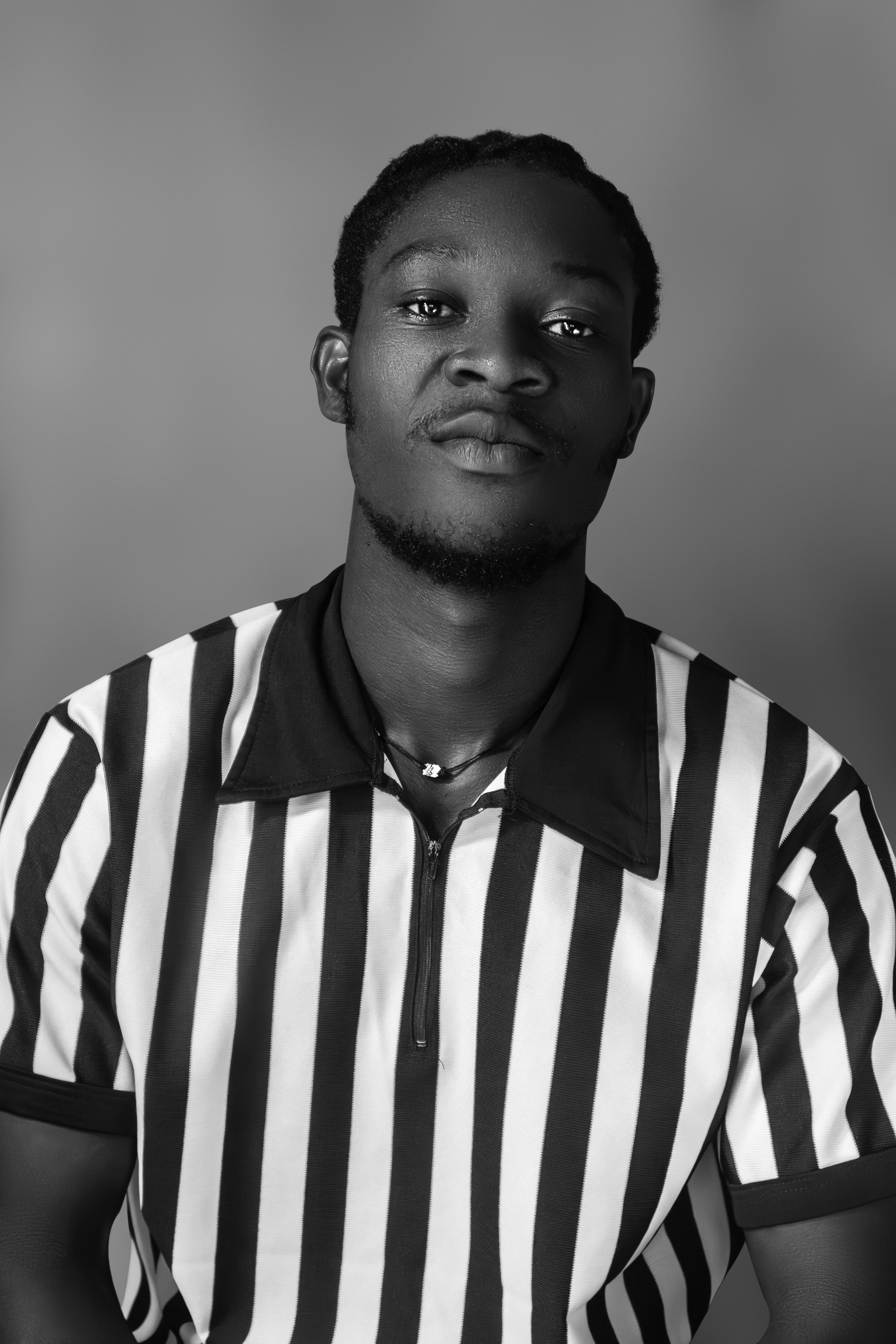 Striking black and white portrait of a man wearing a referee shirt, exuding confidence.