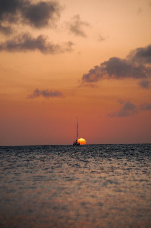 Free A serene scene of a sailboat silhouetted against a stunning ocean sunset. Stock Photo