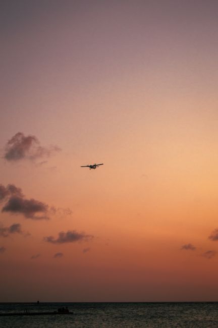 Airplane flies above the ocean at sunset creating a beautiful silhouette against a colorful sky.