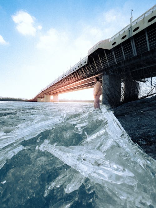 A man standing on the ice next to a bridge