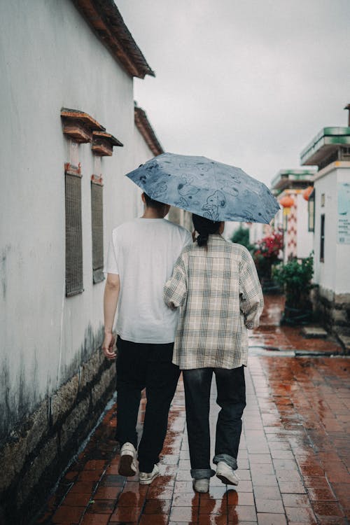 Two people walking down a brick walkway holding an umbrella