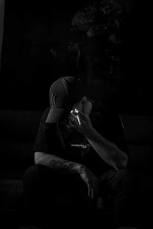 Free Dark Black and White Photo of a Man in a Cap Sitting and Smoking  Stock Photo