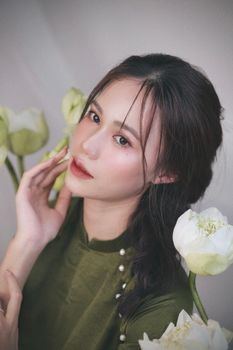 A young woman in a green dress posing elegantly among white flowers indoors.