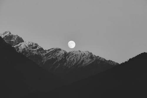A black and white photo of the moon over mountains