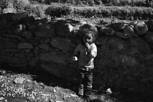 A black and white photo of a child standing in front of a stone wall