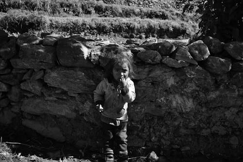 A black and white photo of a child standing in front of a stone wall