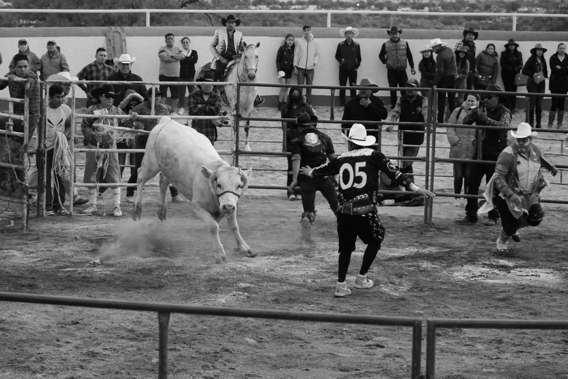 Dynamic black and white image capturing cowboys and a bull at a rodeo event.