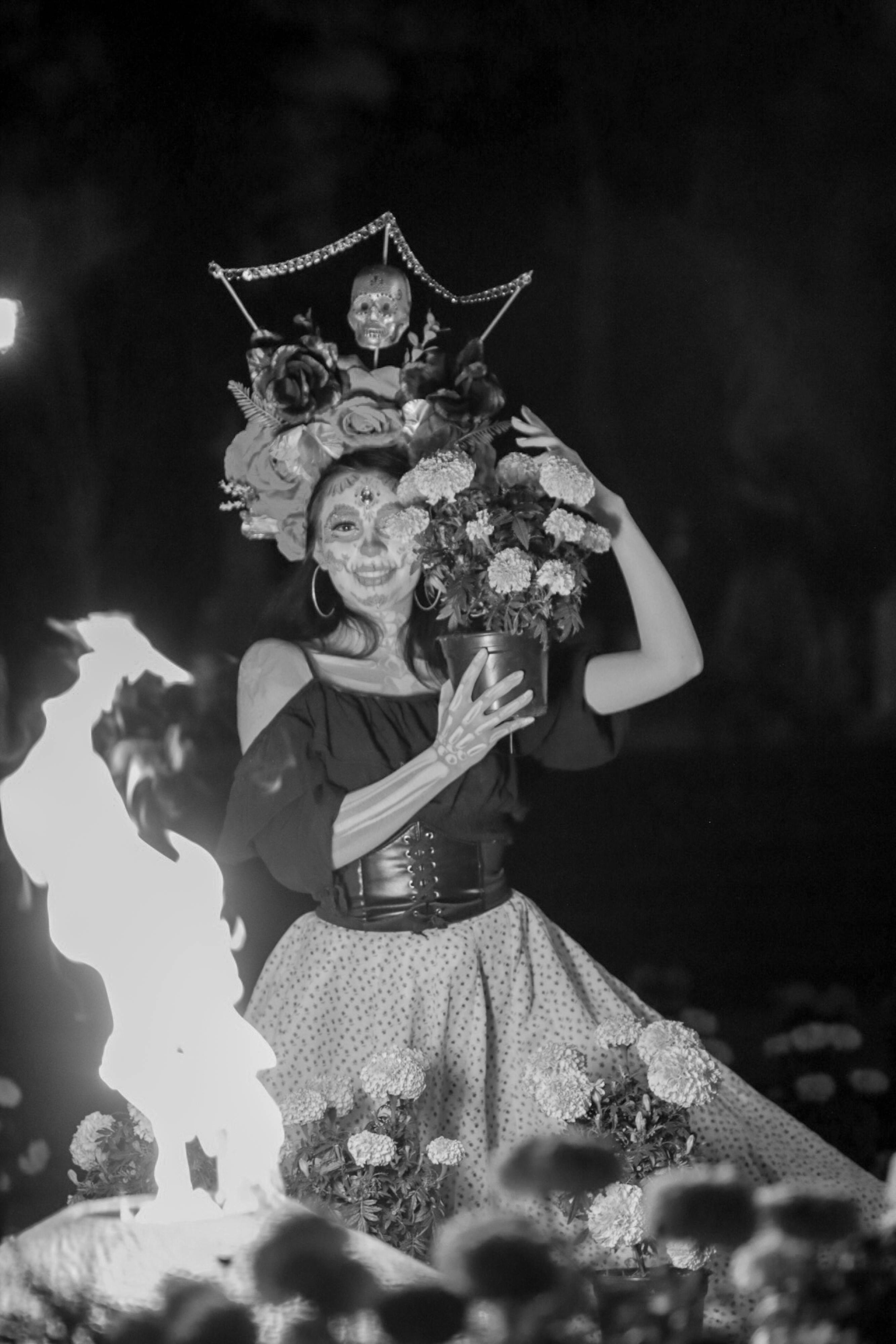 Bezpłatne Uśmiechnięta Catrina Siedząca Z Kwiatami Przy Ogniu W Nocy Zdjęcie z galerii