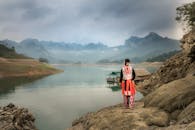 身着传统服装的人站在山间宁静的湖泊旁，四周雾气缭绕，美景天成