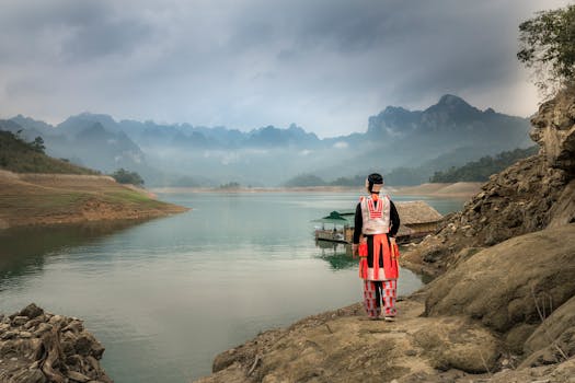 身着传统服装的人站在山间宁静的湖泊旁，四周雾气缭绕，美景天成