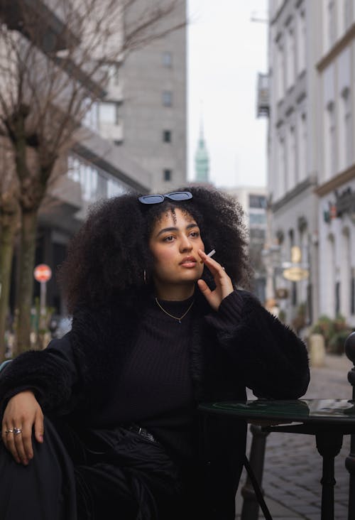 A woman with curly hair sitting on a bench smoking a cigarette