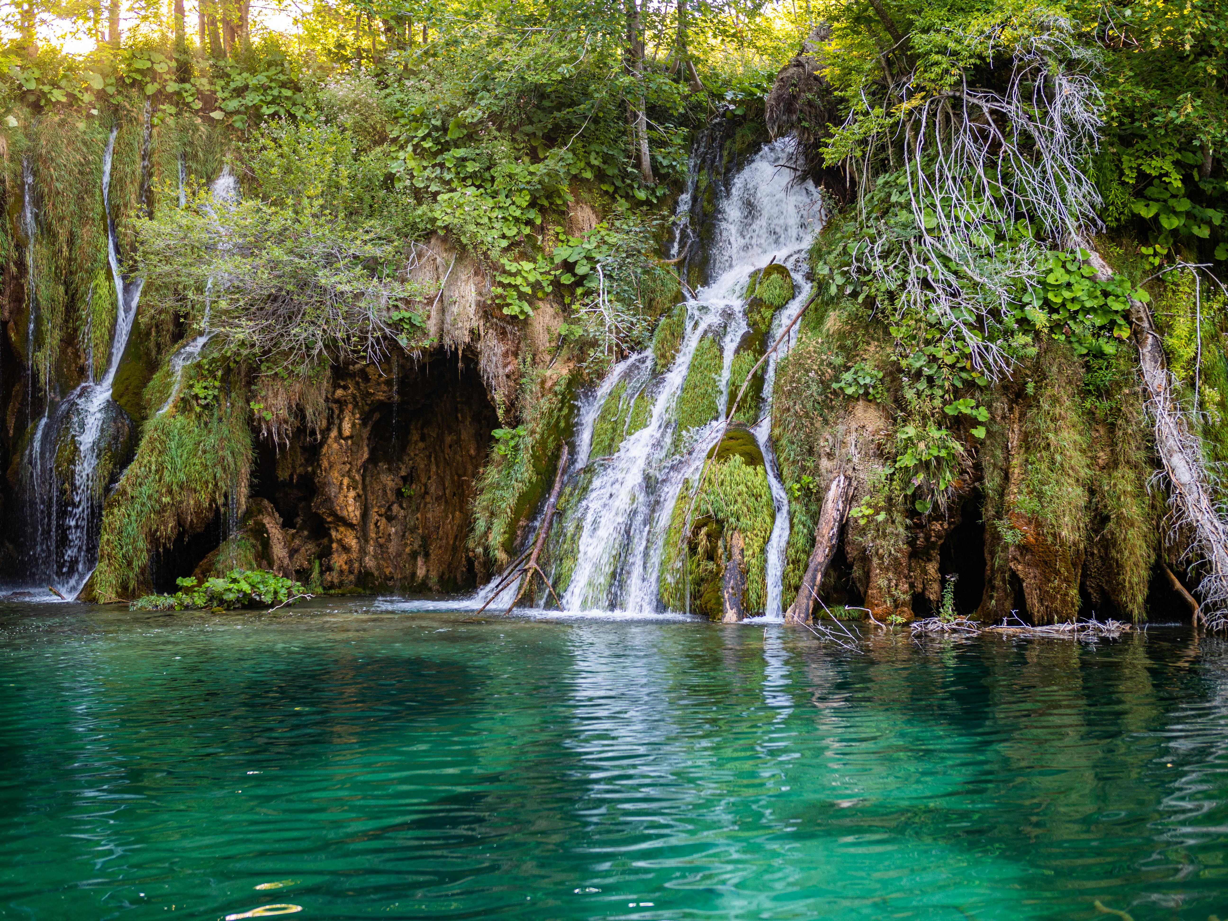 Turquoise cascading waterfalls flowing over travertine barriers through emerald forest at Plitvice Lakes National Park, Croatia