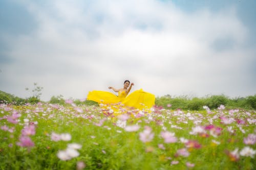 A woman in a yellow dress is sitting on a flower field