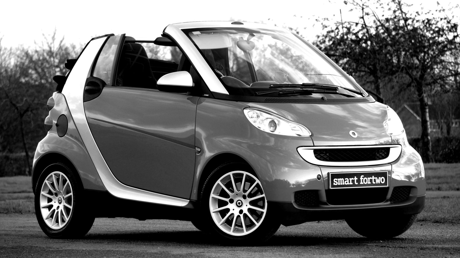 A stylish black and white image of a classic Smart Fortwo convertible parked outdoors.